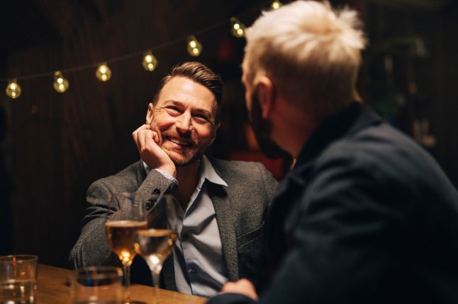 Homme mature souriant s'appuyant sur le coude et écoutant un ami masculin à la boîte de nuit