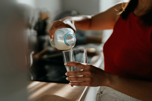 Gros plan d'une femme versant du lait frais du fond à un verre à boire