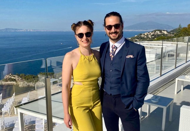 Matt et sa femme en tenue formelle, debout sur un balcon avec la mer derrière eux