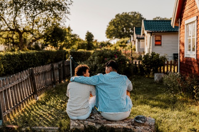 Vue arrière du jeune homme avec un bras autour d'un ami masculin assis sur la connexion dans la cour arrière à Sunny Day