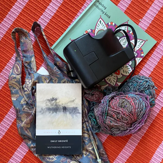 Le contenu du concept de sac analogique d'Eleanor Noyce, comprenant un livre de coloriage, un appareil photo Polaroid, un sac fourre-tout en soie, un exemplaire de Wuthering Heights d'Emily Bronte et du tricot.