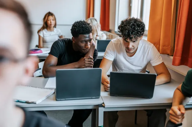 Des lycéens multiraciaux discutant sur un ordinateur portable au bureau en classe