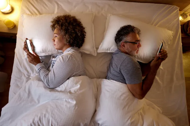 Vue ci-dessus d'un couple d'âge mûr détendu utilisant un téléphone portable au lit.