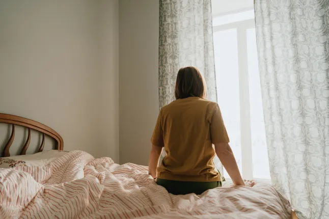 Femme assise sur le lit près de la fenêtre dans la chambre donnant sur la lumière du matin et les rideaux