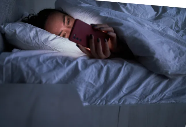Femme envoyant des messages sur un smartphone au lit.