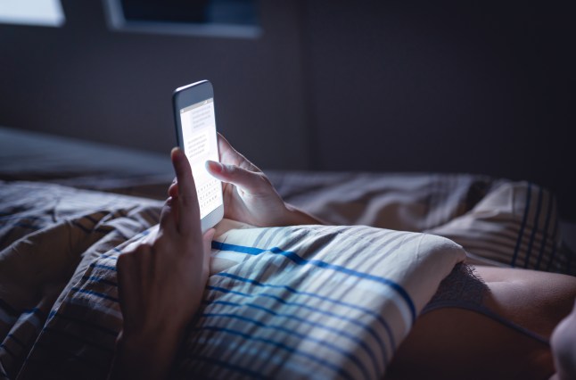 Femme utilisant le téléphone la nuit au lit.