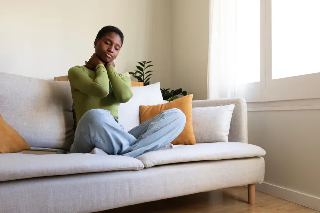 Jeune femme afro-américaine assise sur le canapé en se massant le cou. Femme noire souffrant de douleurs au cou.