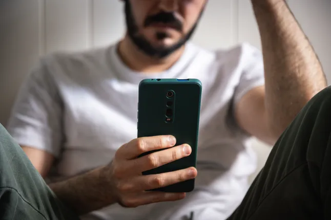 Homme déprimé défilant sur smartphone à la maison.