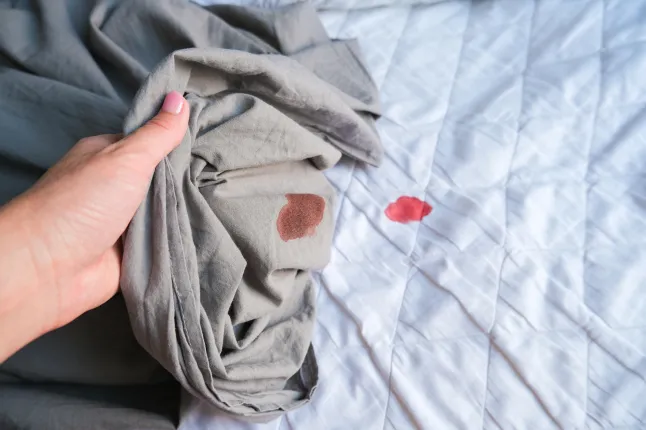 Une tache de sang sur un drap gris/un matelas blanc (Photo : Getty Images)