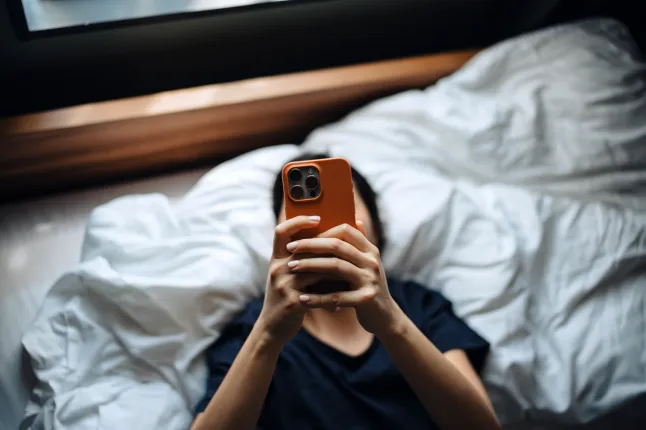 Prise de vue en grand angle d'une femme envoyant des SMS sur son smartphone alors qu'elle est allongée sur son lit.