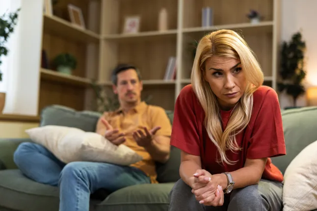 Couple assis sur un canapé avec une personne qui a l'air bouleversée tandis que les autres gestes lors d'une conversation à la maison