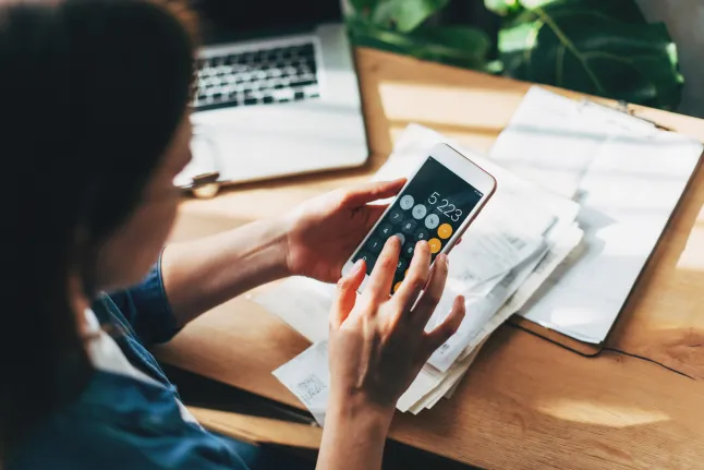 Une femme utilise une calculatrice, un ordinateur et son téléphone pour établir son budget.