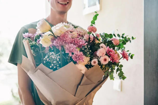 Un jeune homme souriant a livré un bouquet de fleurs chez lui.