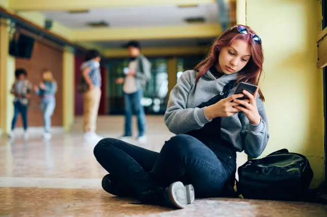 Une adolescente pensive envoie des SMS sur son téléphone portable dans le couloir du lycée.