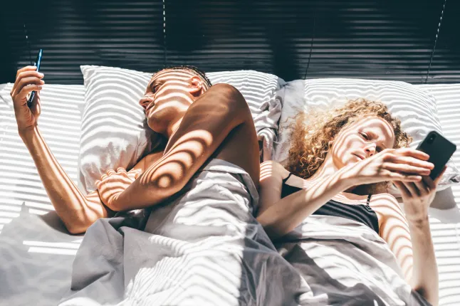 Jeune couple allongé au lit et utilisant un smartphone à la maison.