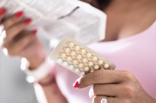 Une femme tient des pilules contraceptives dans une main et des instructions d’utilisation dans l’autre.