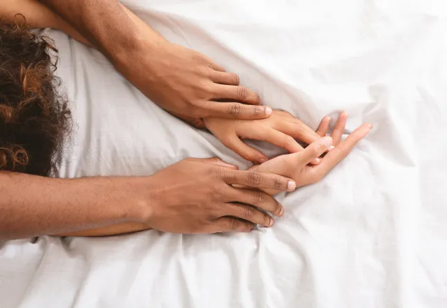Homme et femme se tenant la main pendant qu’ils font l’amour au lit.