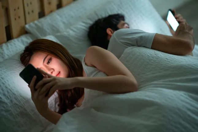 Photo d'un jeune couple utilisant son téléphone portable au lit le matin, dos à dos