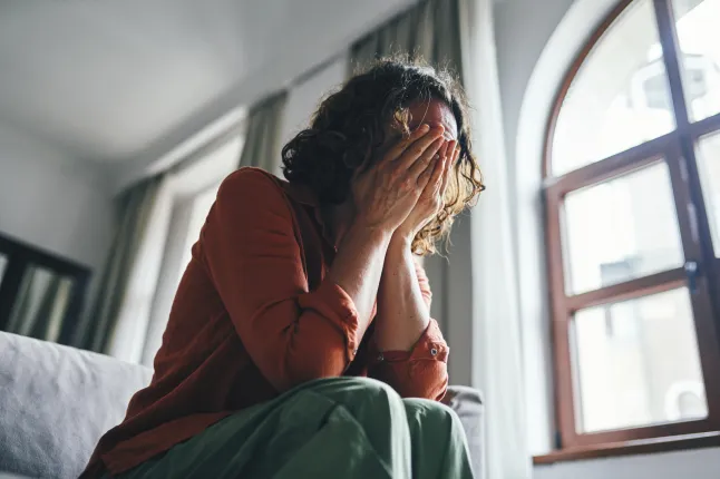 Femme stressée assise à l'intérieur couvrant le visage avec les mains
