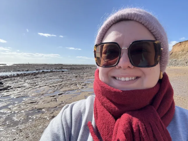 Emma Flint sourit dehors, portant une écharpe rouge et des lunettes noires