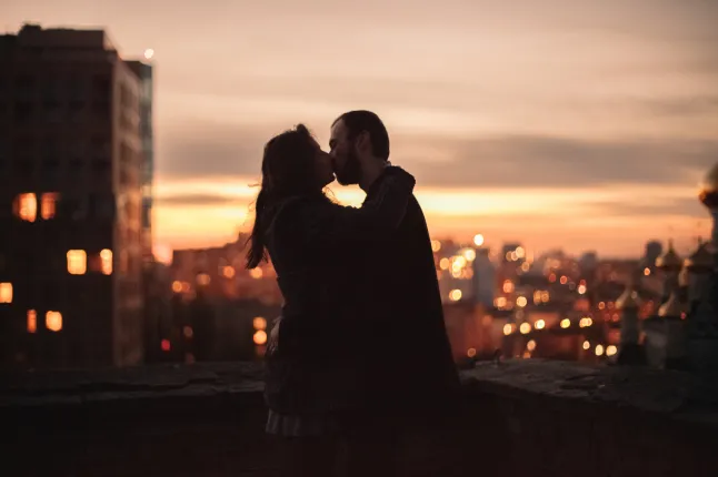 Jeune couple s'embrassant debout sur le toit urbain le soir