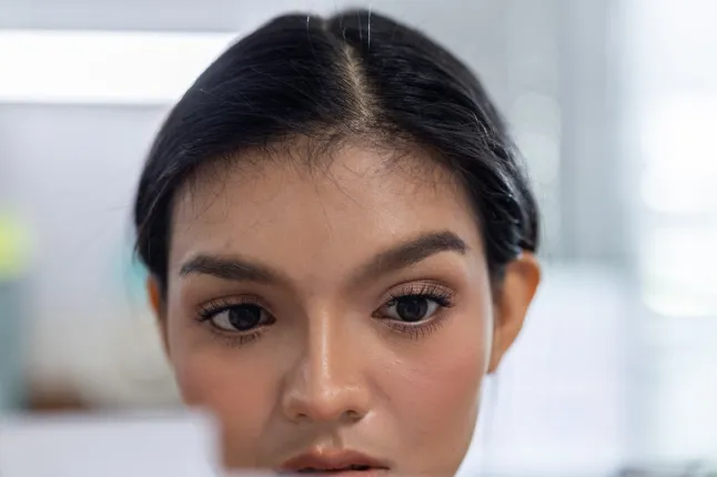 Femme visage oeil portrait cheveux noirs intérieur gros plan maquillage, visage de jeune femme concentré avec oeil sombre et beauté naturelle dans une pièce lumineuse