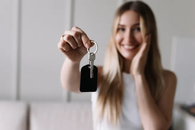 Une jeune femme joyeuse au sourire éclatant tient un jeu de clés alors qu'elle rencontre un agent immobilier à l'entrée de son nouvel appartement.