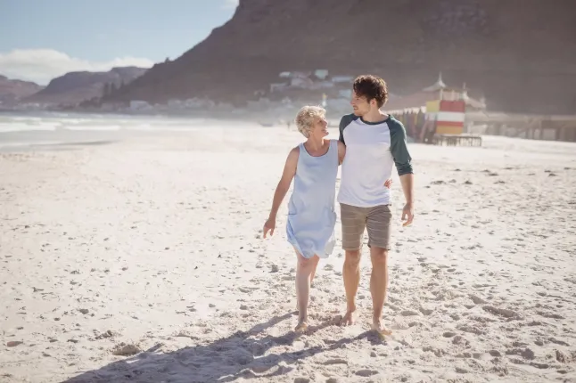 Jeune homme avec sa mère marchant sur le sable à la plage pendant la journée ensoleillée