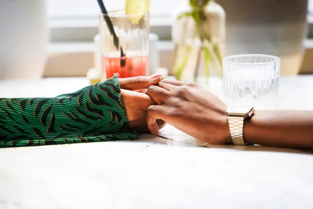 Deux individus se tiennent la main autour d’une table, exprimant un sentiment de confort et de proximité dans un cadre détendu.