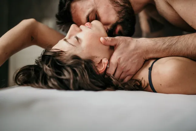 Photo vue latérale d'un beau couple au lit, doux et sensuel. Un beau mec avec une barbe sur la belle brune lui embrasse le cou pendant que ses yeux sont fermés. Faire l'amour