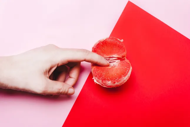 Une main pique un morceau de pamplemousse sur un fond rose et rouge.