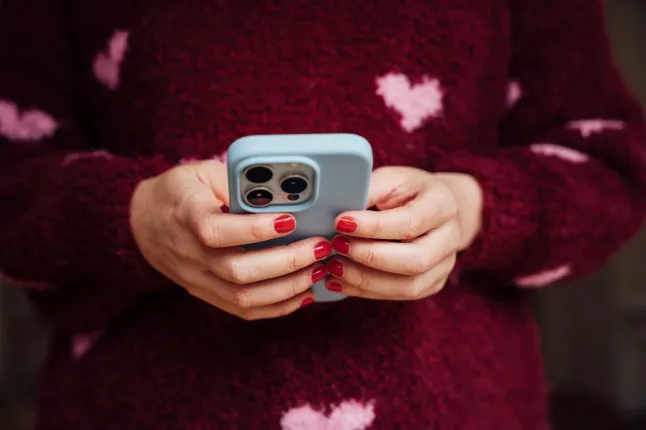 Gros plan de mains féminines tenant et tapant sur un smartphone moderne.