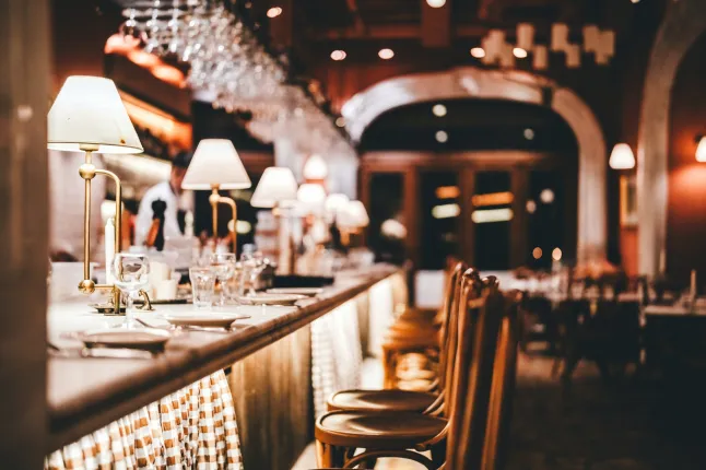 Comptoir de bar de restaurant élégant avec un éclairage tamisé, de la verrerie et des chaises en bois, créant une atmosphère de restauration chaleureuse et raffinée. L'image symbolise l'hospitalité, la gastronomie, la vie nocturne et un style de vie moderne.