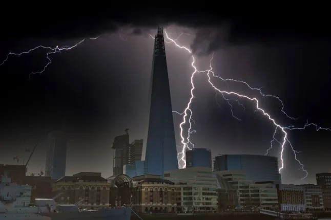 Un paysage urbain nocturne représentant le Shard à Londres, en Angleterre, est considérablement illuminé par plusieurs éclairs lors d'un orage. Des nuages ​​sombres remplissent la partie supérieure du cadre.