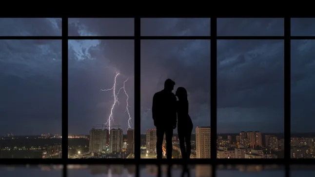 L’homme et la femme debout près d’une fenêtre panoramique regardant la foudre