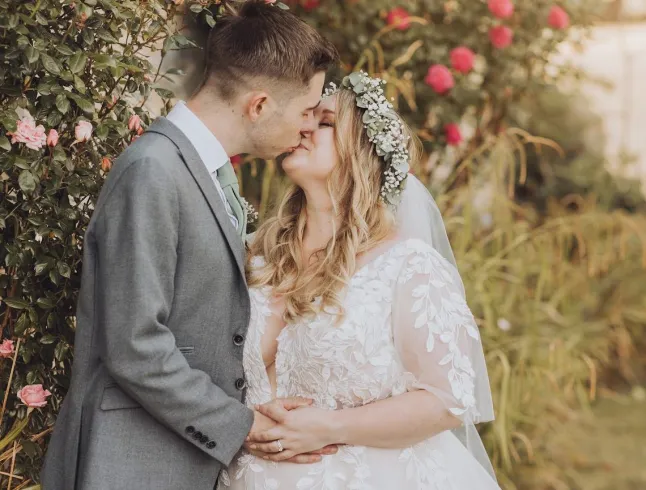 Laura Clarke embrassant son mari le jour de leur mariage, beaucoup de feuillage en arrière-plan