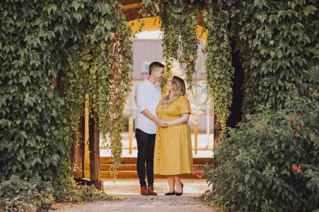 Laura Clarke et son fiancé d'alors, debout, se tenant la main et se regardant dans les yeux sous une arcade avec beaucoup de feuillage vert