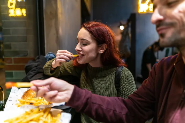 Jeune couple affamé mangeant de délicieux hamburgers et des frites dans un restaurant de restauration rapide, riant et s'amusant