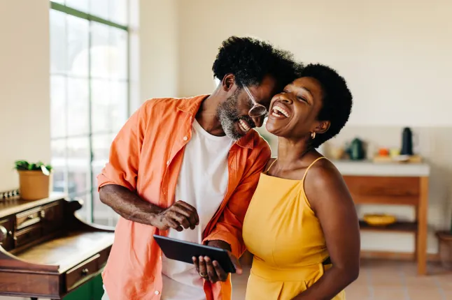 Heureux couple d'âge mûr riant et s'amusant avec une tablette à la maison