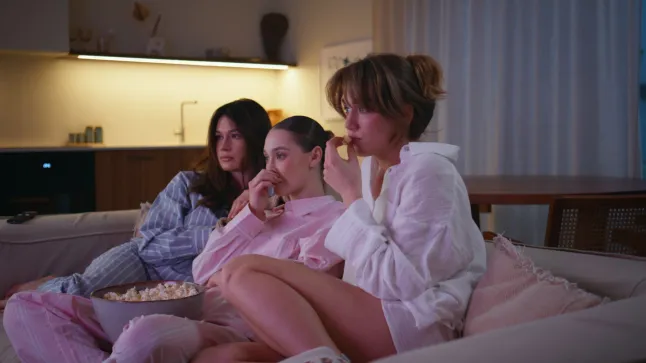 Des filles concentrées regardent un film en mangeant du pop-corn lors d'une fête à la maison en pyjama. Trois femmes sérieuses regardant un film télévisé sérieux dans un appartement du soir. Des amies allongées sur un canapé profitent d'une collation. Notion d'amitié