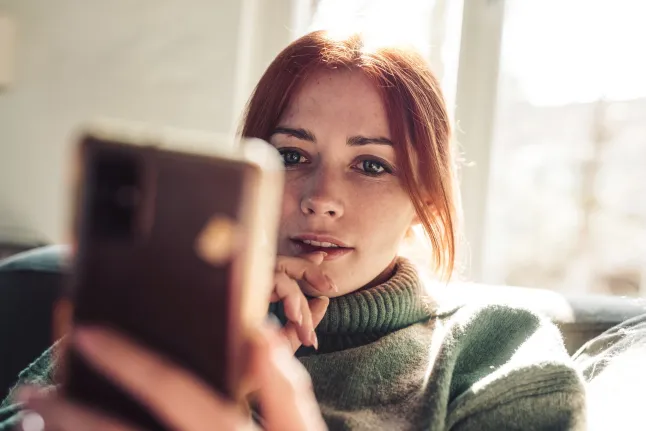 Femme aux cheveux rouges regardant l'écran de son téléphone portable.
