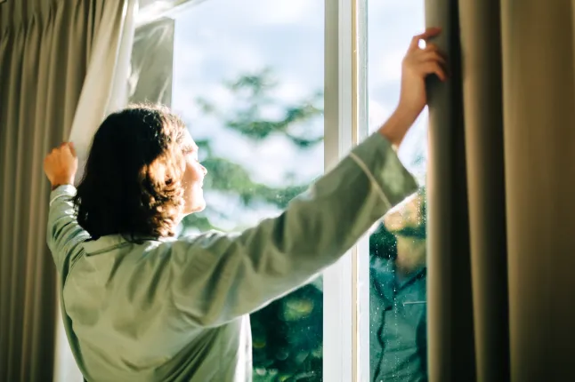Femme ouvrant les rideaux sentant la lumière du soleil du matin