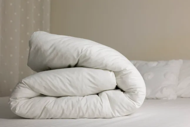Couette pliée douce sur un lit dans une chambre confortable. Intérieur confortable avec literie propre et espace de copie.